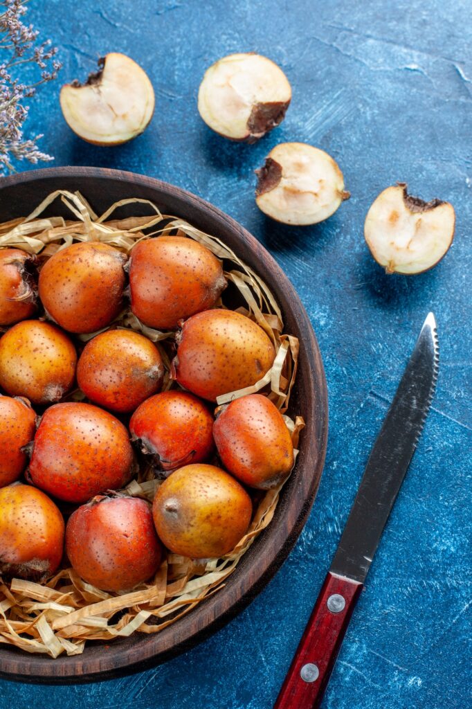 vertical view of whole and chopped mespilus germanica inside and outside a brown bowl next to fork